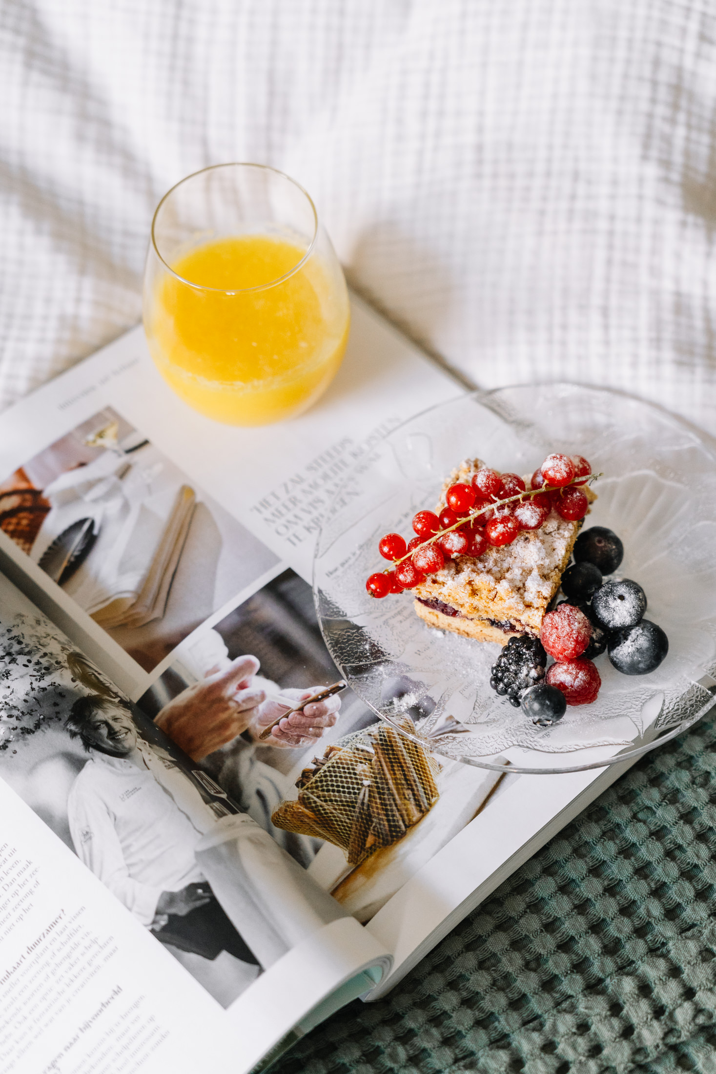 Zoete lekkernij en glas jus d'orange op tijdschrift in tweepersoonsbed van Kamer Comfort Deluxe